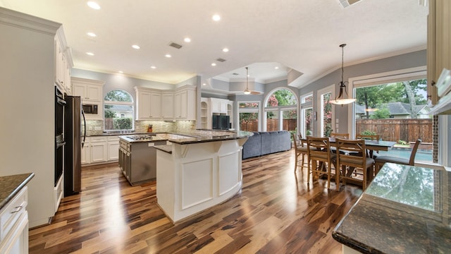 kitchen with visible vents, backsplash, open floor plan, wood finished floors, and dark stone counters