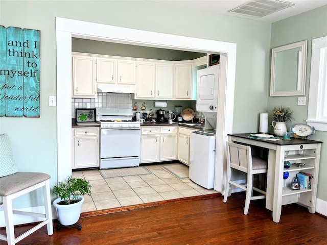 kitchen featuring dark countertops, visible vents, under cabinet range hood, white range with gas cooktop, and stacked washer / drying machine