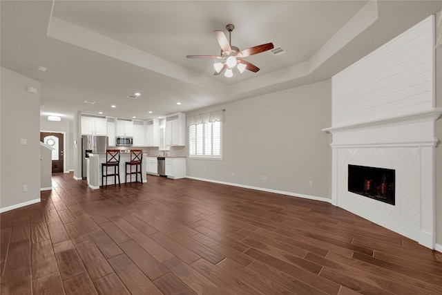 unfurnished living room with a tray ceiling, dark wood-style flooring, a tiled fireplace, and baseboards