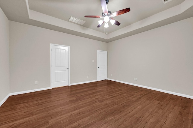 unfurnished room with ceiling fan, wood finished floors, visible vents, baseboards, and a tray ceiling