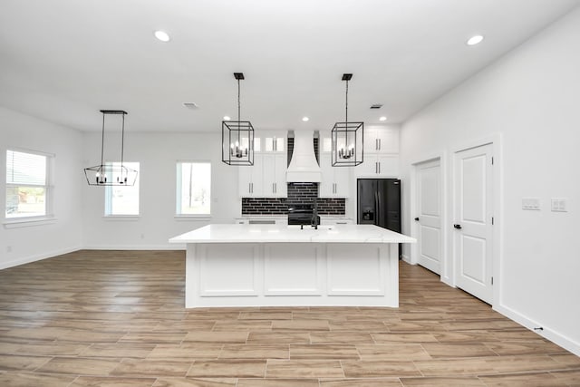 kitchen with black fridge with ice dispenser, light wood-style flooring, backsplash, white cabinets, and premium range hood