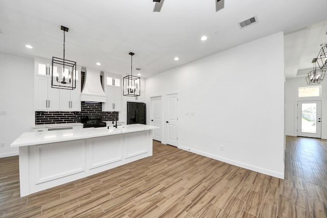 kitchen featuring a chandelier, visible vents, backsplash, black appliances, and custom range hood