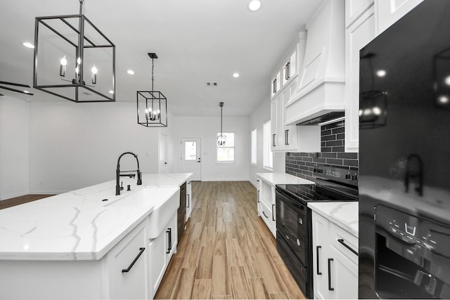 kitchen with white cabinets, decorative backsplash, black appliances, light wood finished floors, and custom range hood