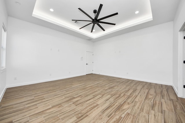 unfurnished room with light wood-style floors, a tray ceiling, and a ceiling fan