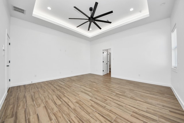 spare room featuring a ceiling fan, a tray ceiling, and light wood-type flooring