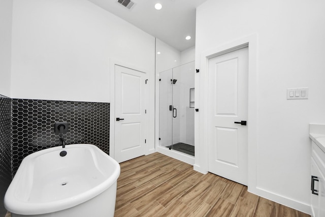 bathroom with a soaking tub, visible vents, wood finished floors, and a stall shower