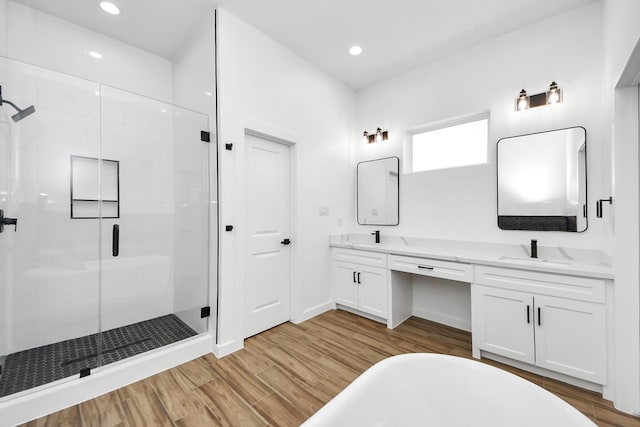 full bathroom featuring double vanity, a stall shower, a sink, wood finished floors, and a freestanding tub