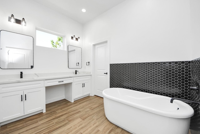 full bathroom with a freestanding tub, wood finished floors, a sink, and double vanity