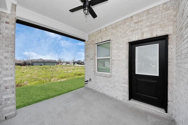 view of exterior entry featuring a yard, ceiling fan, and brick siding