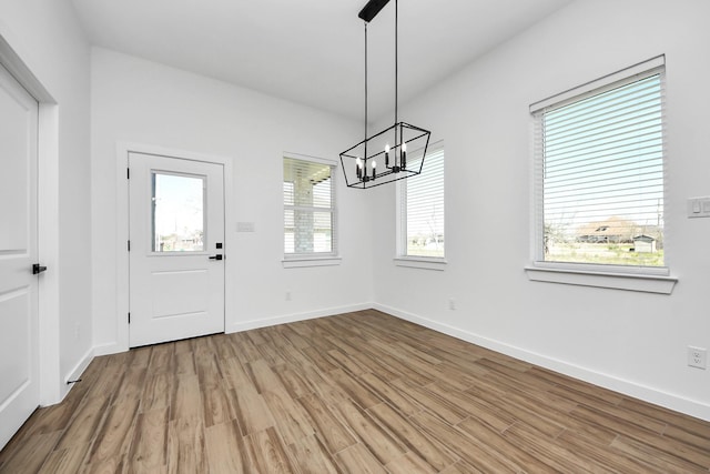 unfurnished dining area with a notable chandelier, baseboards, and wood finished floors