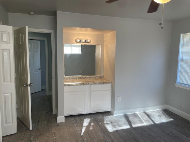 interior space featuring dark wood finished floors, white cabinetry, ceiling fan, light stone countertops, and baseboards