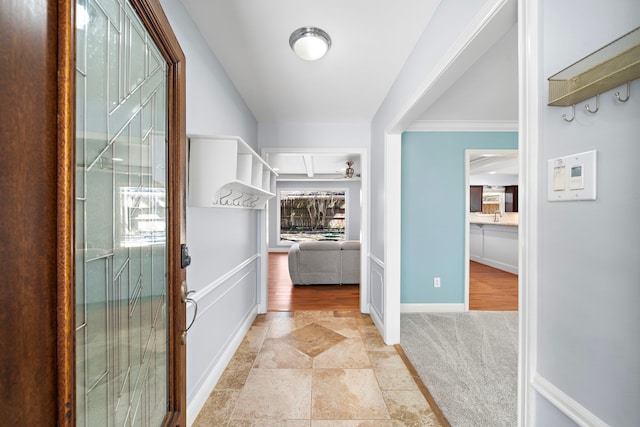 hallway featuring stone finish floor, baseboards, a sink, and light colored carpet