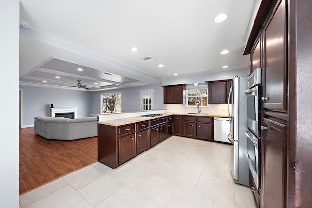 kitchen featuring a fireplace, open floor plan, dark brown cabinetry, a sink, and ceiling fan