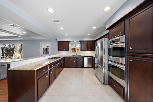 kitchen with stainless steel appliances, a peninsula, a sink, visible vents, and light stone countertops