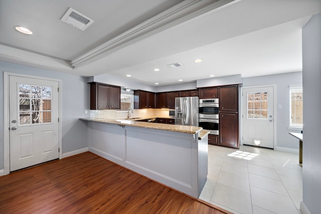 kitchen with a peninsula, a sink, visible vents, appliances with stainless steel finishes, and light stone countertops