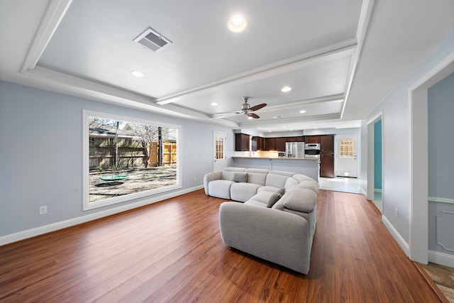 living room featuring a tray ceiling, visible vents, recessed lighting, and wood finished floors