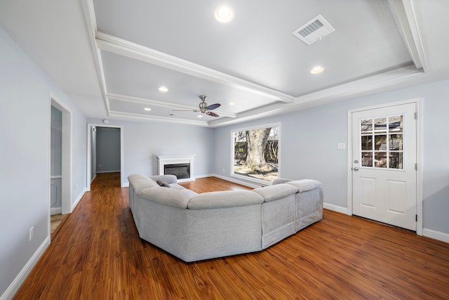 living room with baseboards, visible vents, a raised ceiling, a glass covered fireplace, and wood finished floors