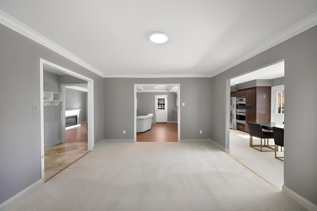 unfurnished living room with ornamental molding, a glass covered fireplace, light colored carpet, and baseboards