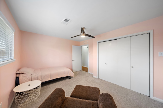 bedroom with baseboards, visible vents, light colored carpet, ceiling fan, and a closet