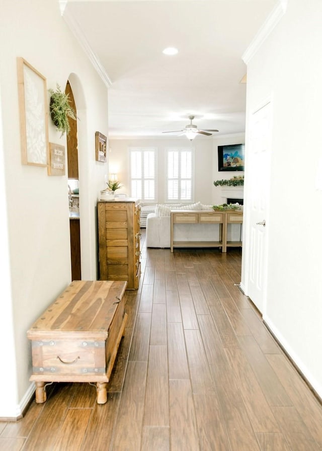 interior space featuring wood finish floors, crown molding, arched walkways, and baseboards