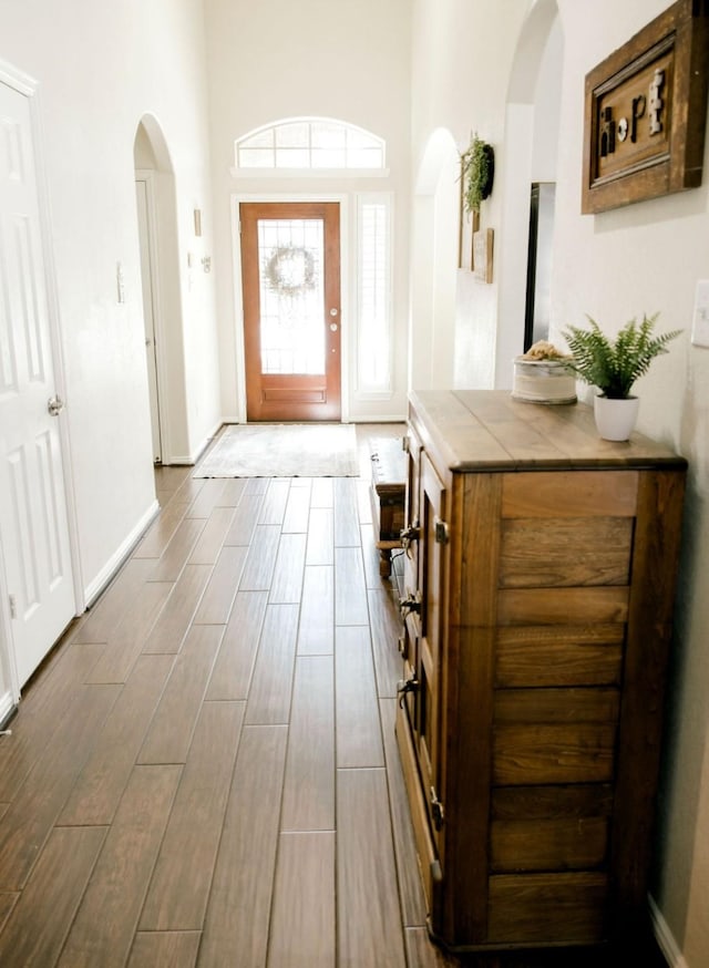 foyer featuring wood tiled floor, arched walkways, and baseboards