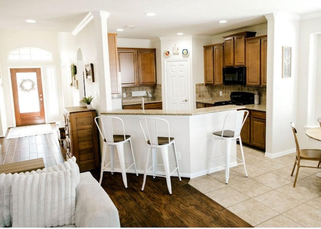 kitchen featuring a breakfast bar area, a peninsula, brown cabinets, black appliances, and crown molding