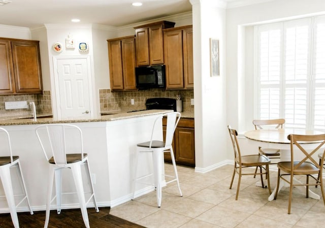 kitchen featuring brown cabinetry, black microwave, a kitchen breakfast bar, and crown molding