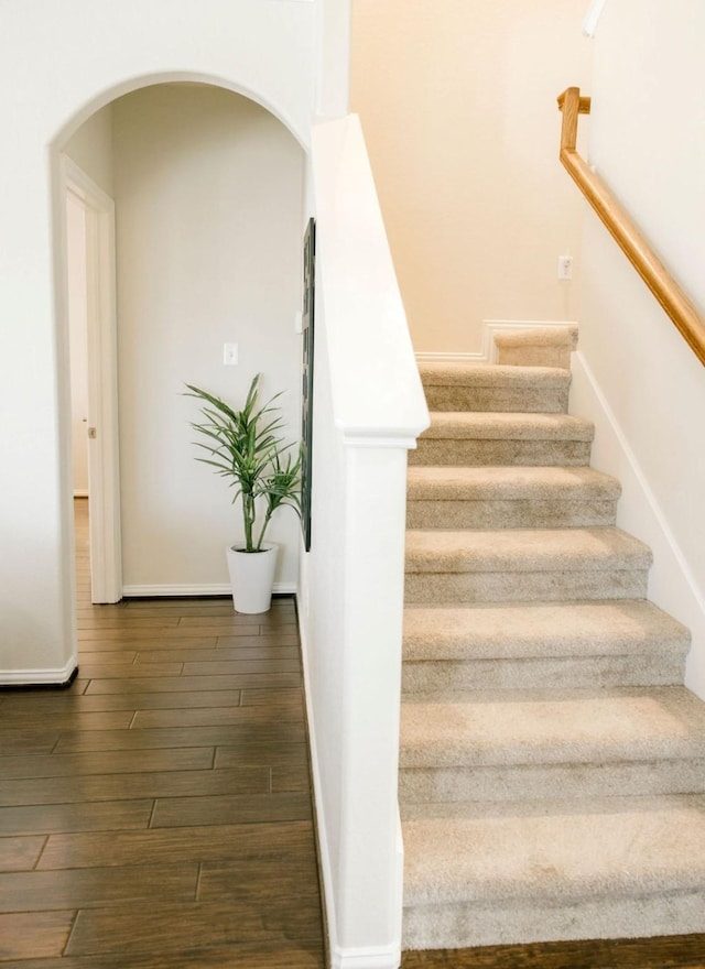 staircase with baseboards, arched walkways, and wood finished floors