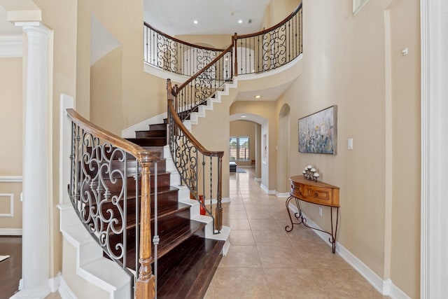 entryway with arched walkways, tile patterned flooring, a towering ceiling, baseboards, and decorative columns