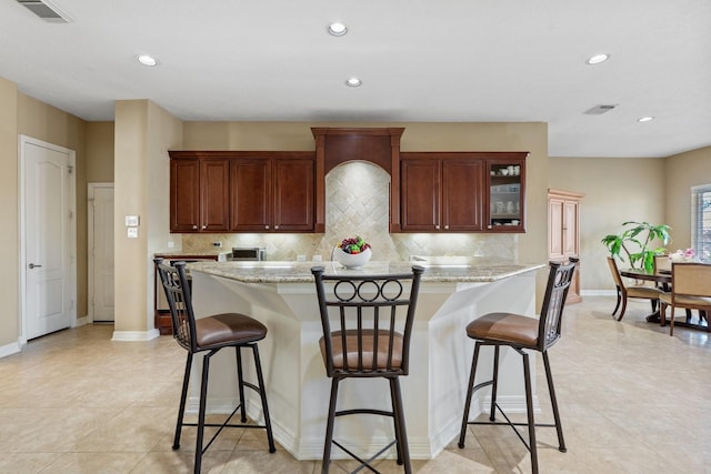 kitchen featuring decorative backsplash, visible vents, glass insert cabinets, and a kitchen breakfast bar