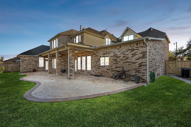 back of property at dusk featuring brick siding, a lawn, a patio area, and fence