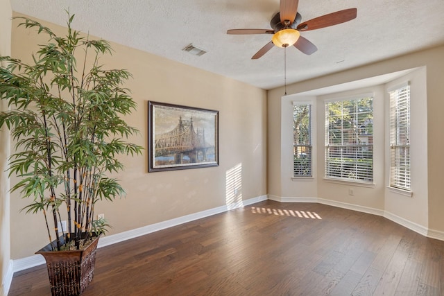 unfurnished room featuring a textured ceiling, dark wood-style flooring, visible vents, and baseboards