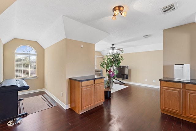 home office with ceiling fan, dark wood-style flooring, visible vents, baseboards, and vaulted ceiling