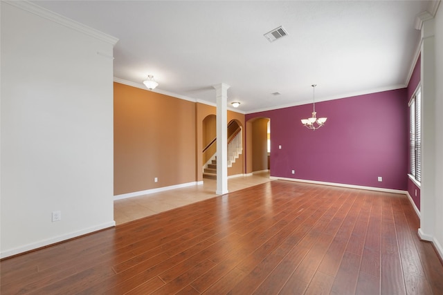 empty room with arched walkways, crown molding, visible vents, wood finished floors, and baseboards