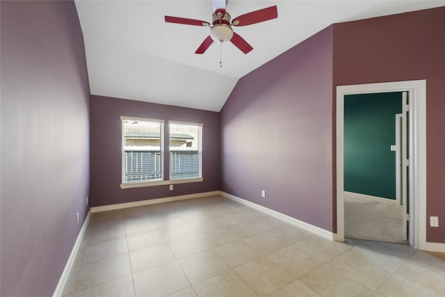 empty room featuring a ceiling fan, vaulted ceiling, baseboards, and light tile patterned floors