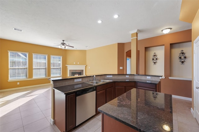 kitchen featuring visible vents, stainless steel dishwasher, a sink, a large island with sink, and a lit fireplace