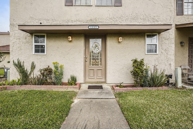 entrance to property featuring a lawn and stucco siding