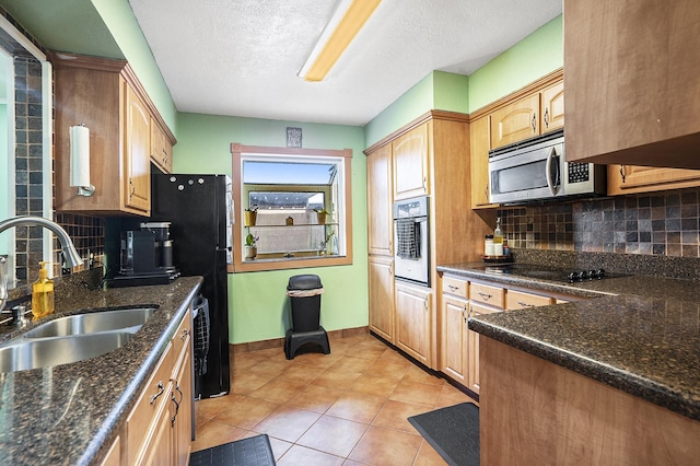 kitchen featuring dark stone counters, black appliances, backsplash, and a sink