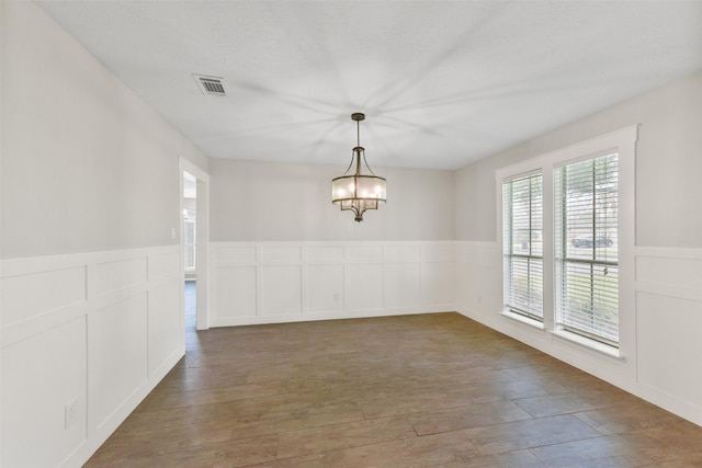 unfurnished dining area featuring visible vents, wood finished floors, a chandelier, and a wainscoted wall