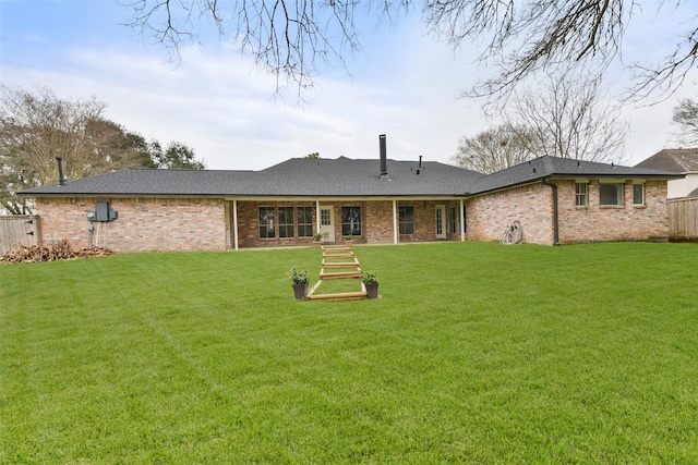 rear view of property with a lawn, brick siding, and fence