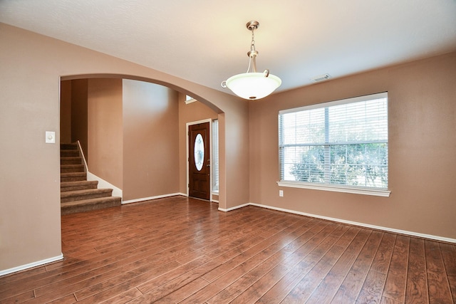 foyer with stairs, visible vents, arched walkways, and wood finished floors