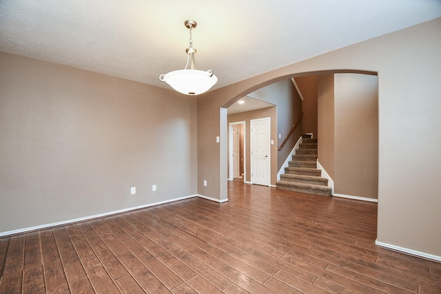 empty room featuring arched walkways, stairway, baseboards, and wood finished floors