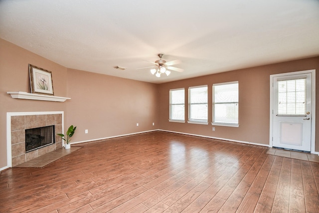 unfurnished living room featuring wood finished floors, a tile fireplace, visible vents, and a ceiling fan
