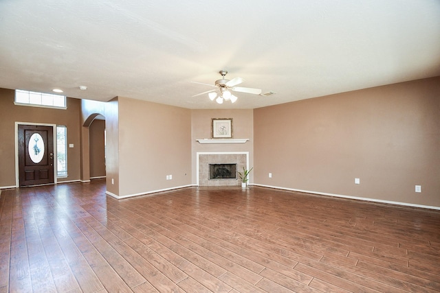 unfurnished living room featuring arched walkways, ceiling fan, a fireplace, and wood finished floors