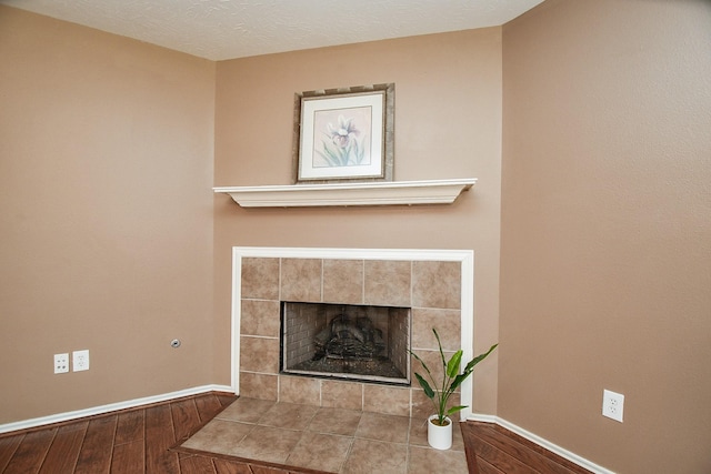details with a tile fireplace, a textured ceiling, baseboards, and wood finished floors