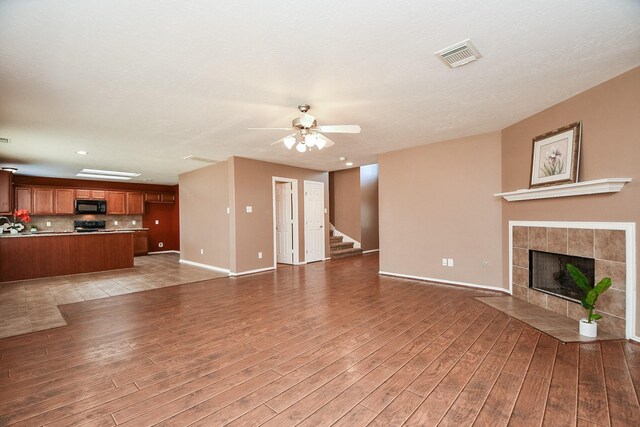 unfurnished living room featuring visible vents, a ceiling fan, a tiled fireplace, stairs, and light wood-style floors