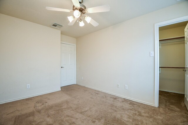 unfurnished bedroom featuring carpet, a closet, visible vents, a spacious closet, and a ceiling fan