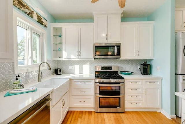 kitchen featuring stacked washer and dryer, light countertops, appliances with stainless steel finishes, light wood-style floors, and white cabinetry