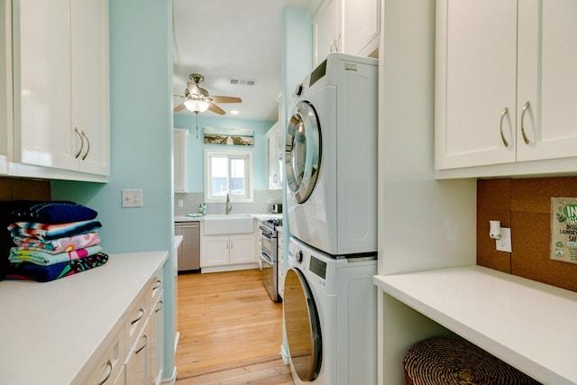 clothes washing area with cabinet space, a ceiling fan, light wood-style flooring, stacked washer / drying machine, and a sink