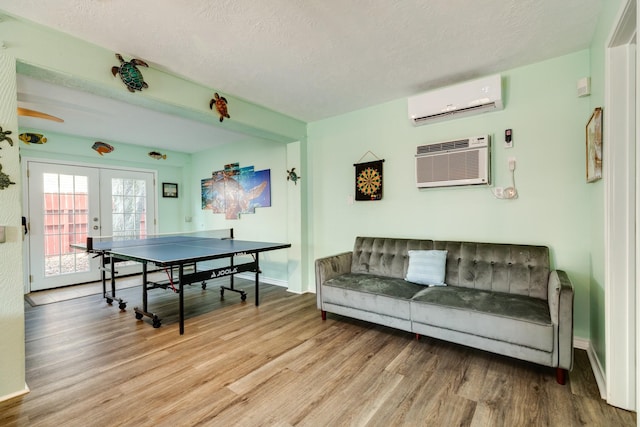 rec room with light wood finished floors, a textured ceiling, french doors, and a wall mounted air conditioner